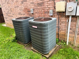 Two AC condenser units against the outside wall of a home–AC & Heat Solutions values customer comfort above all else.